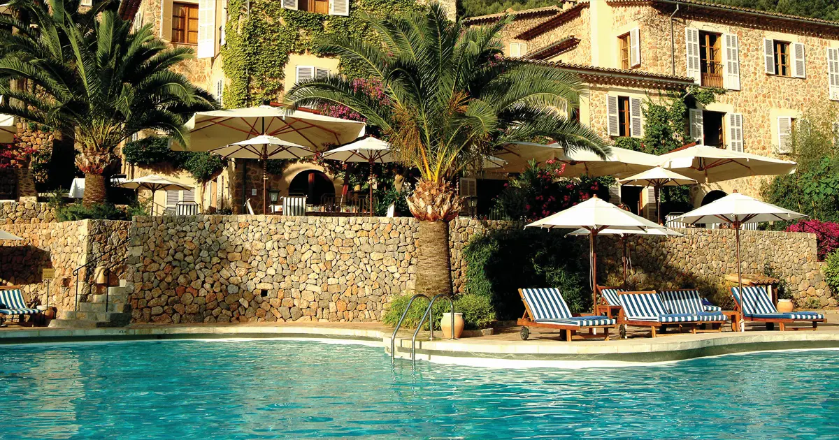 Piscina y fachada de piedra del Hotel Belmond La Residencia en Deia Mallorca con sombrillas y palmeras
