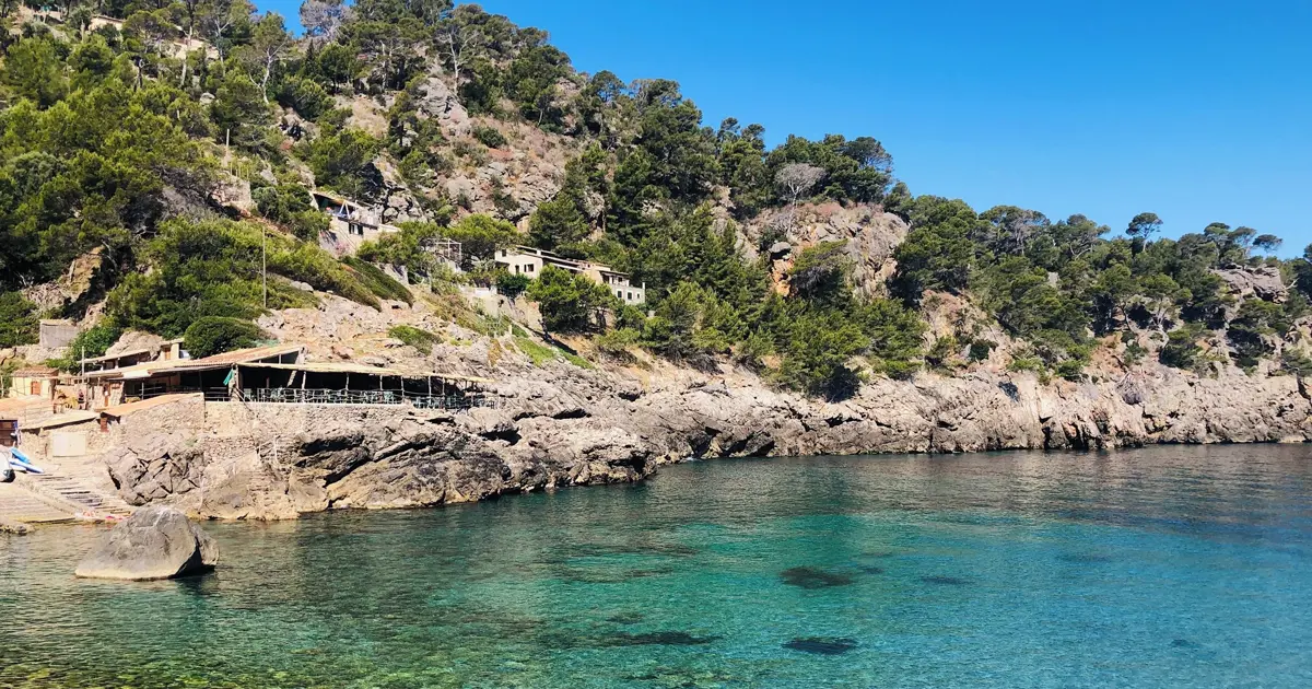 Cala de piedra con embarcaderos y terraza de restaurante en el litoral de Deià