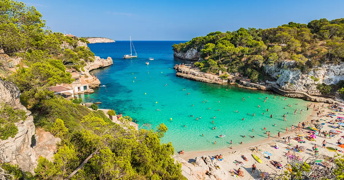 Vista panorámica de la bahía turquesa y acantilados arbolados de Cala Llombards