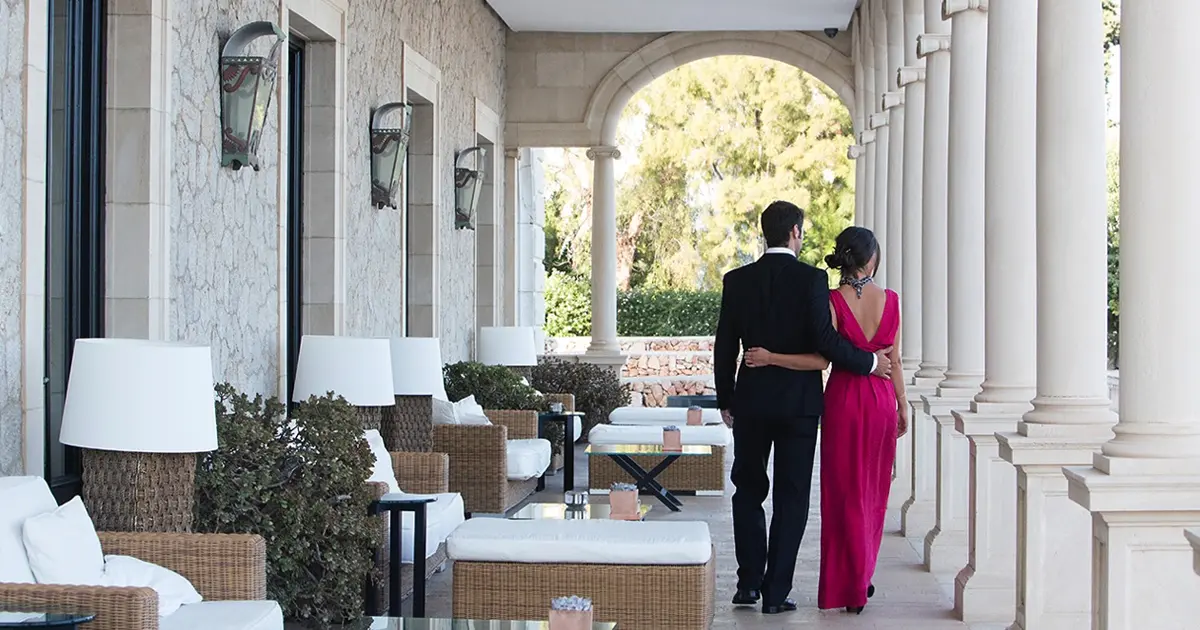 Pareja elegante paseando por la terraza de arcos y columnas de un hotel romántico en Mallorca