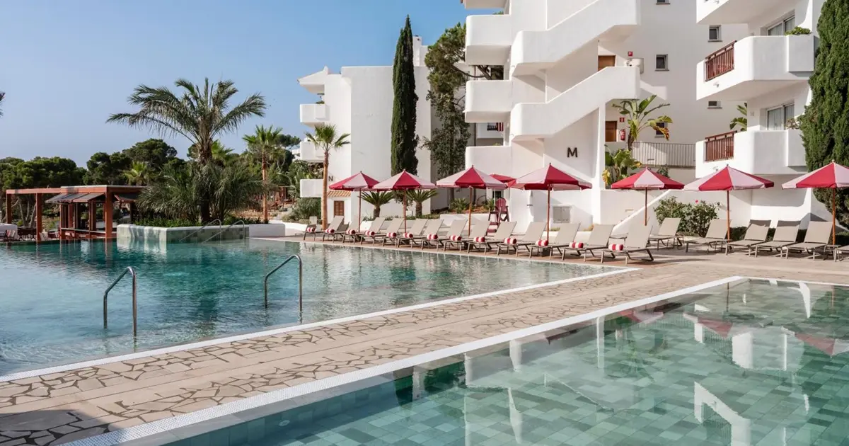Piscina exterior con sombrillas rojas frente a los edificios blancos de Inturotel Es Esmeralda