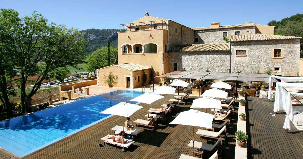 Piscina exterior con solarium de madera y fachada del antiguo monasterio Son Brull Hotel y Spa en Pollenca